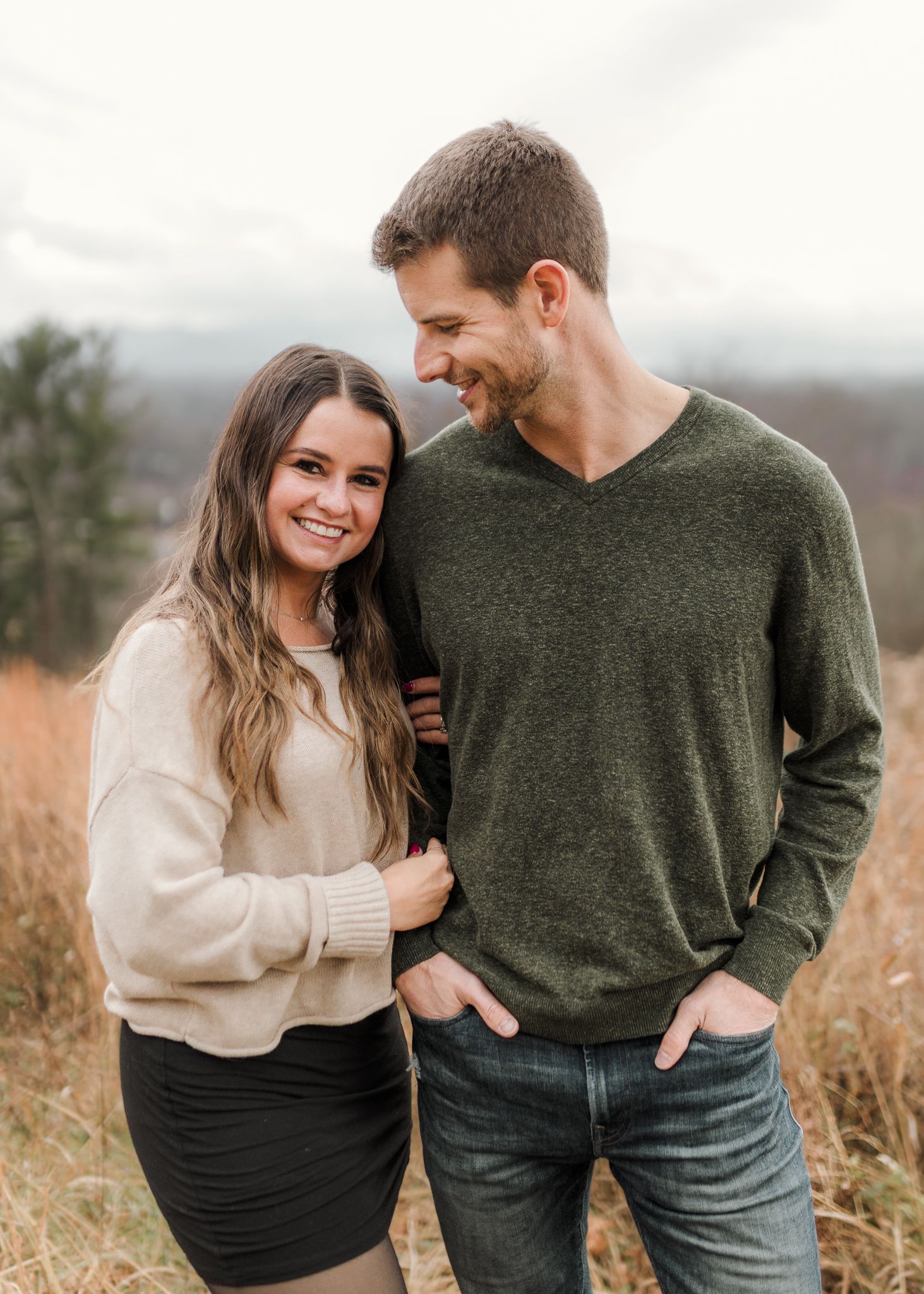 A couple shares intimate moments in a field wearing green and cream sweaters during an outdoor photoshoot.