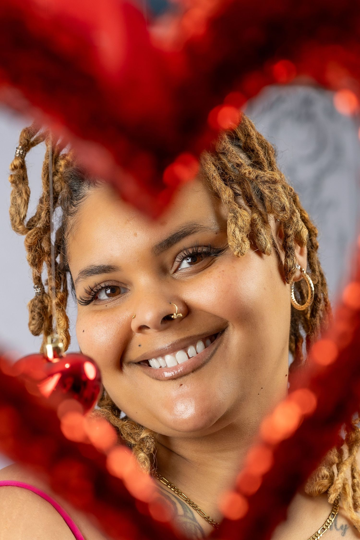 Portrait against red bokeh background with warm lighting and styled blonde dreadlocks.