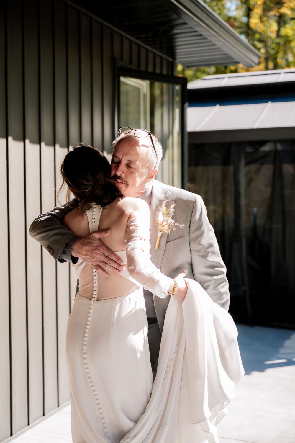 A romantic wedding couple shares a tender kiss against a white building exterior in natural sunlight.