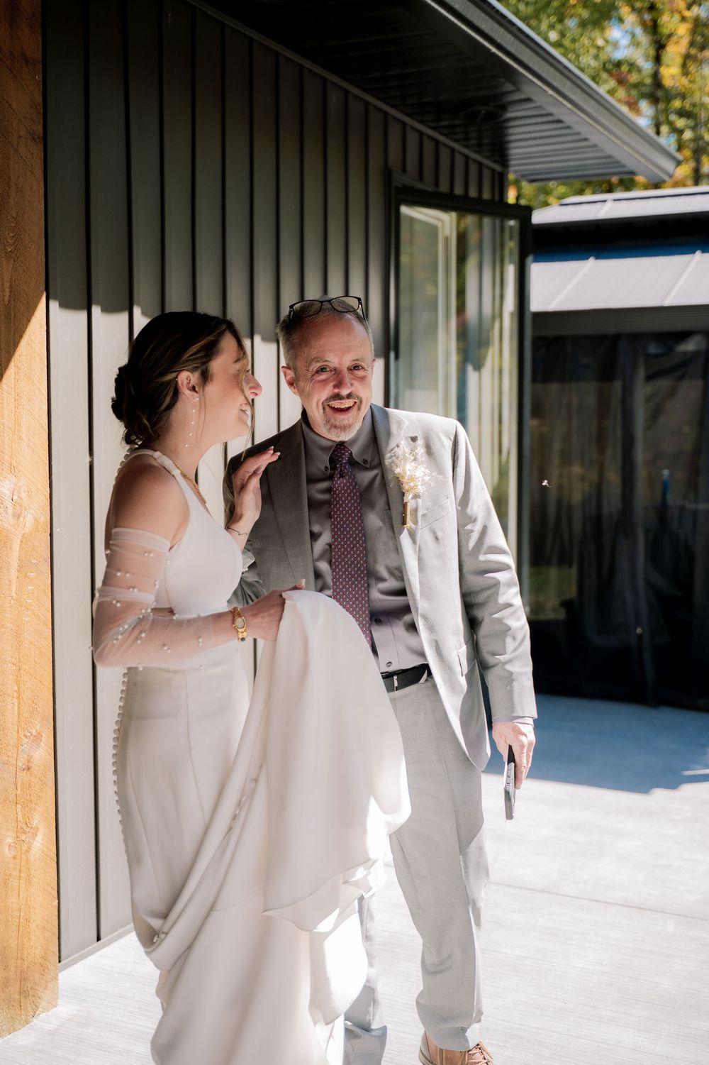 A couple shares a tender moment on a covered porch with wooden posts and white walls.