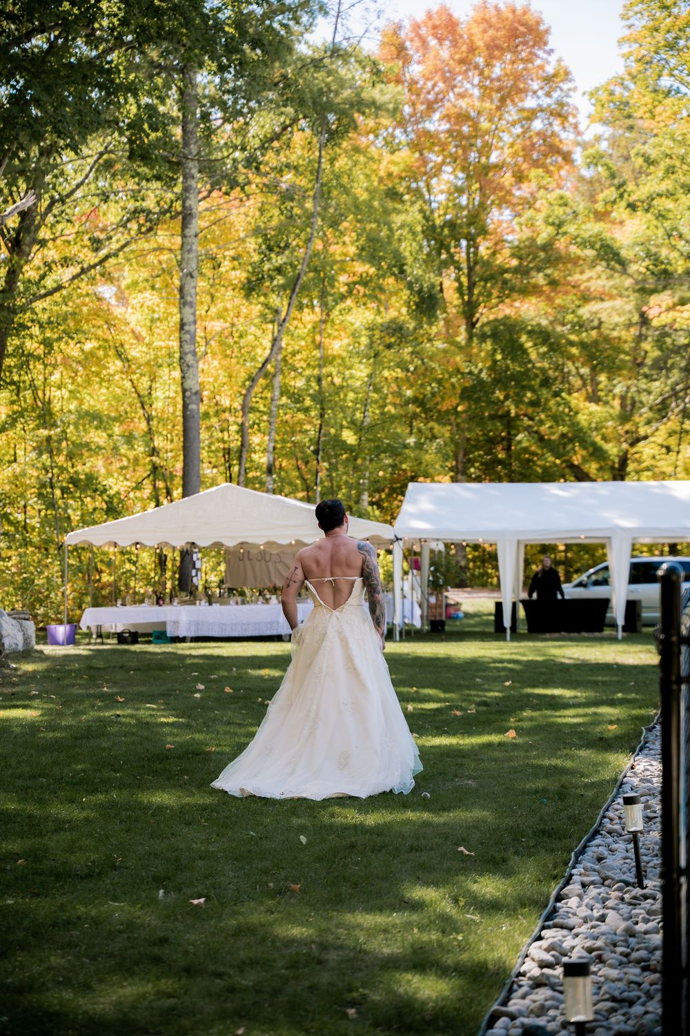 Outdoor wedding setup with white tents and chairs surrounded by autumn trees with golden foliage.