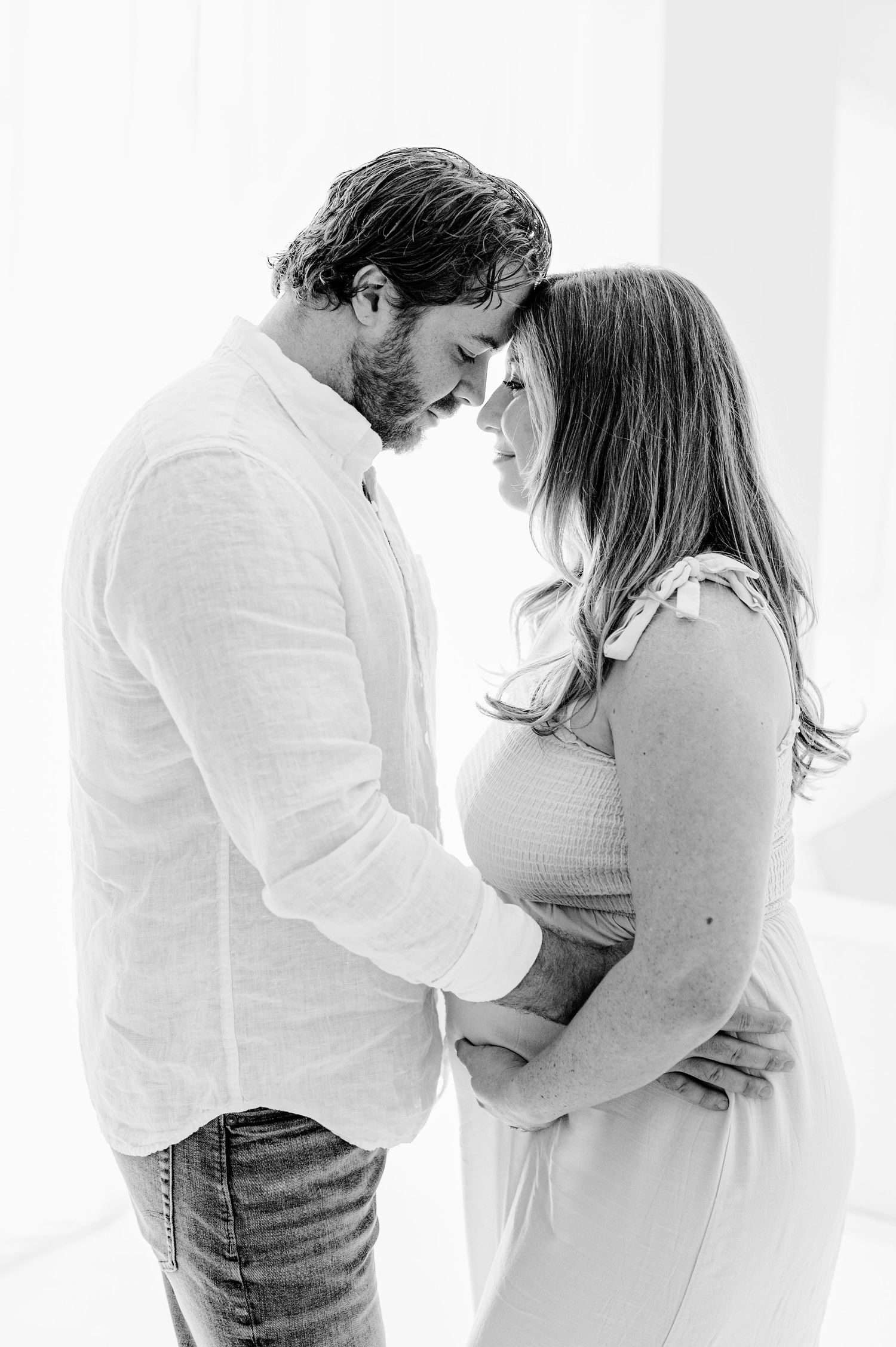 Pregnancy photography in Jacksonville, Fl with mama-to-be in white dress showing couple resting foreheads together.