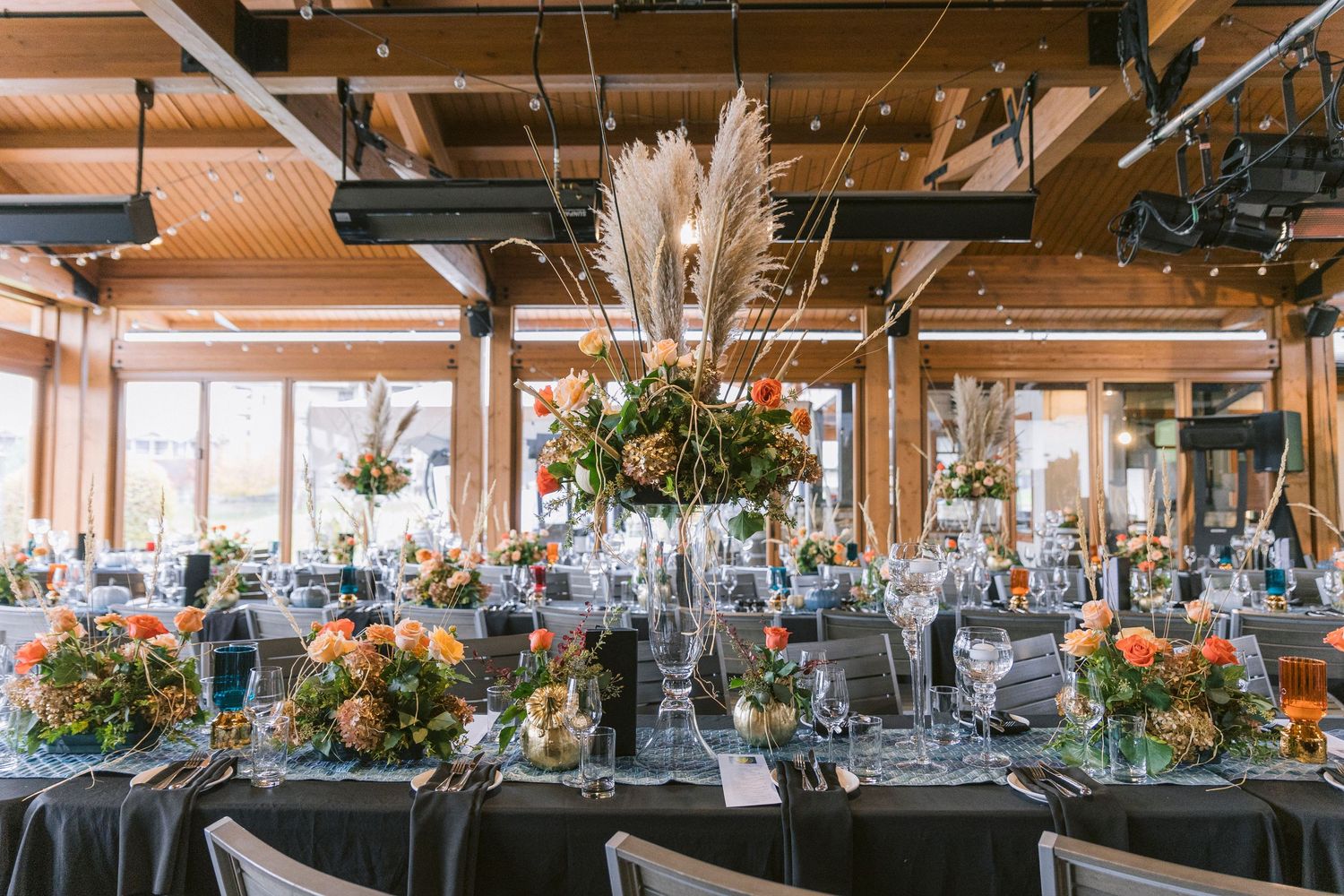 Elegant wedding reception venue with pampas grass centerpieces, charcoal linens and industrial-chic exposed ceiling details.