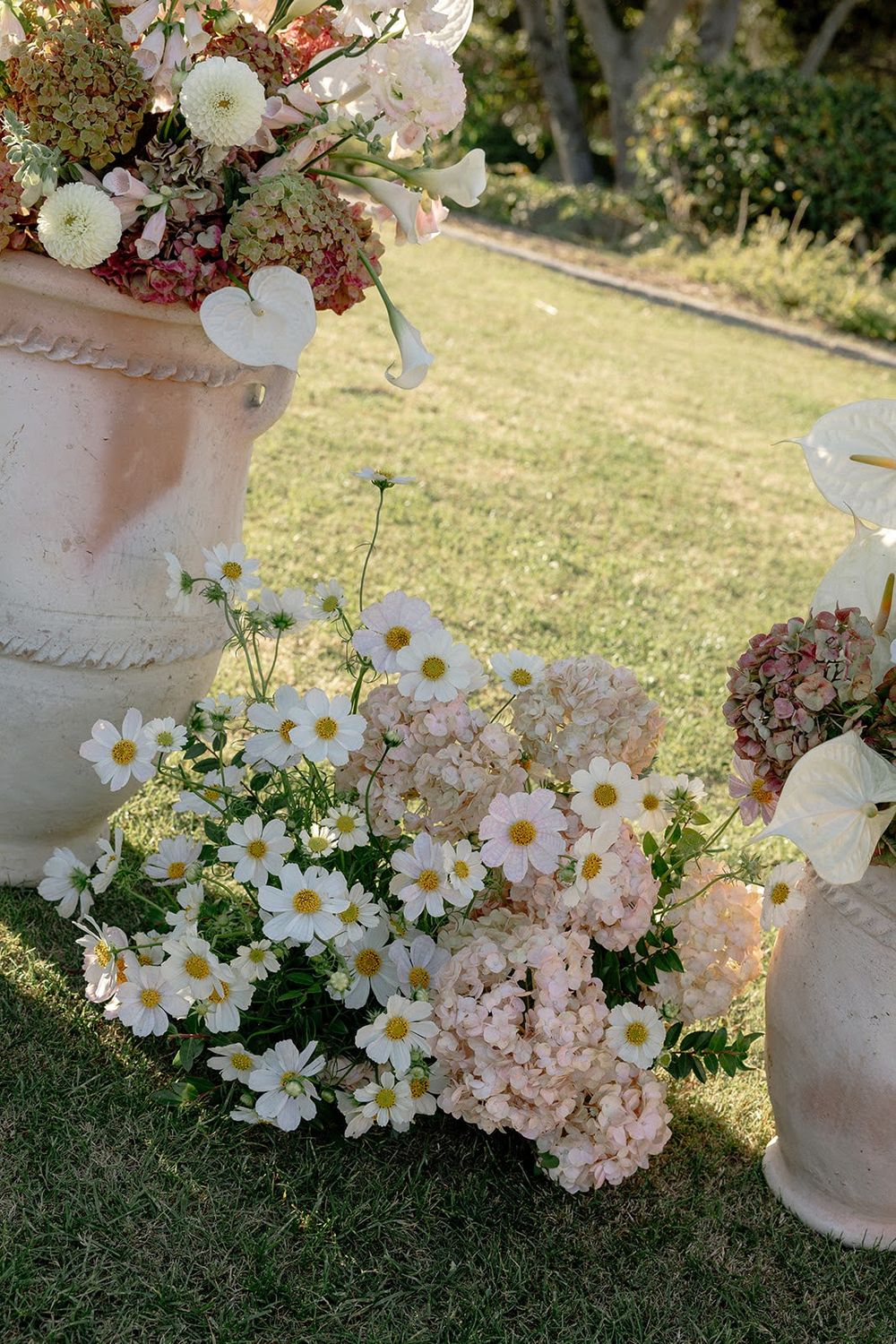 Garden-style flower arrangements featuring daisies and hydrangeas in concrete planters on grass.