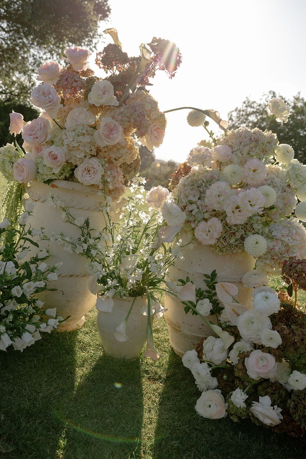 White floral arrangements cascade beautifully against a sunlit garden backdrop creating an ethereal wedding setting.
