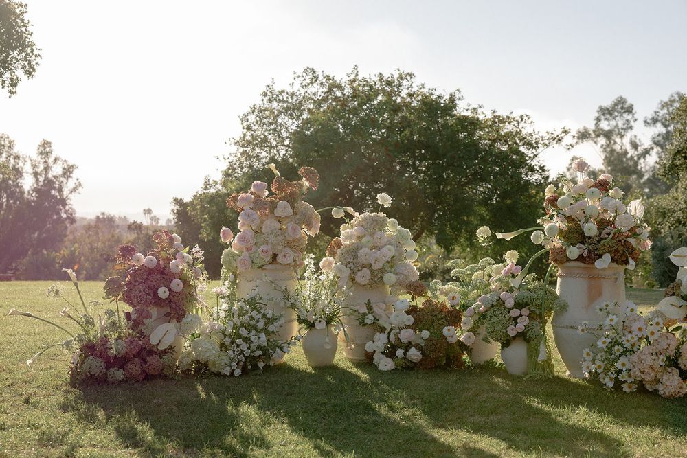 Garden wedding ceremony setup with white floral arrangements and natural greenery at sunset.
