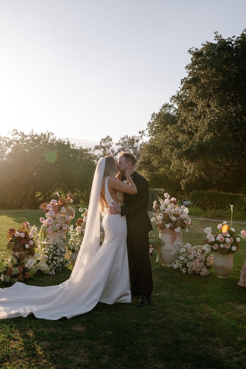 Romantic sunset wedding photos with couple embracing outdoors among floral arrangements.