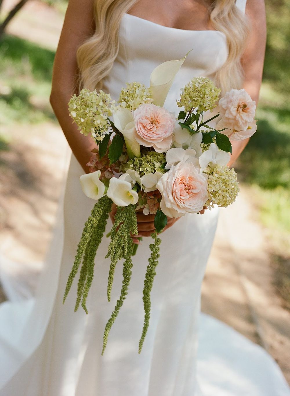 Elegant bridal bouquet featuring blush roses, white calla lilies and cascading amaranthus against a white wedding dress.