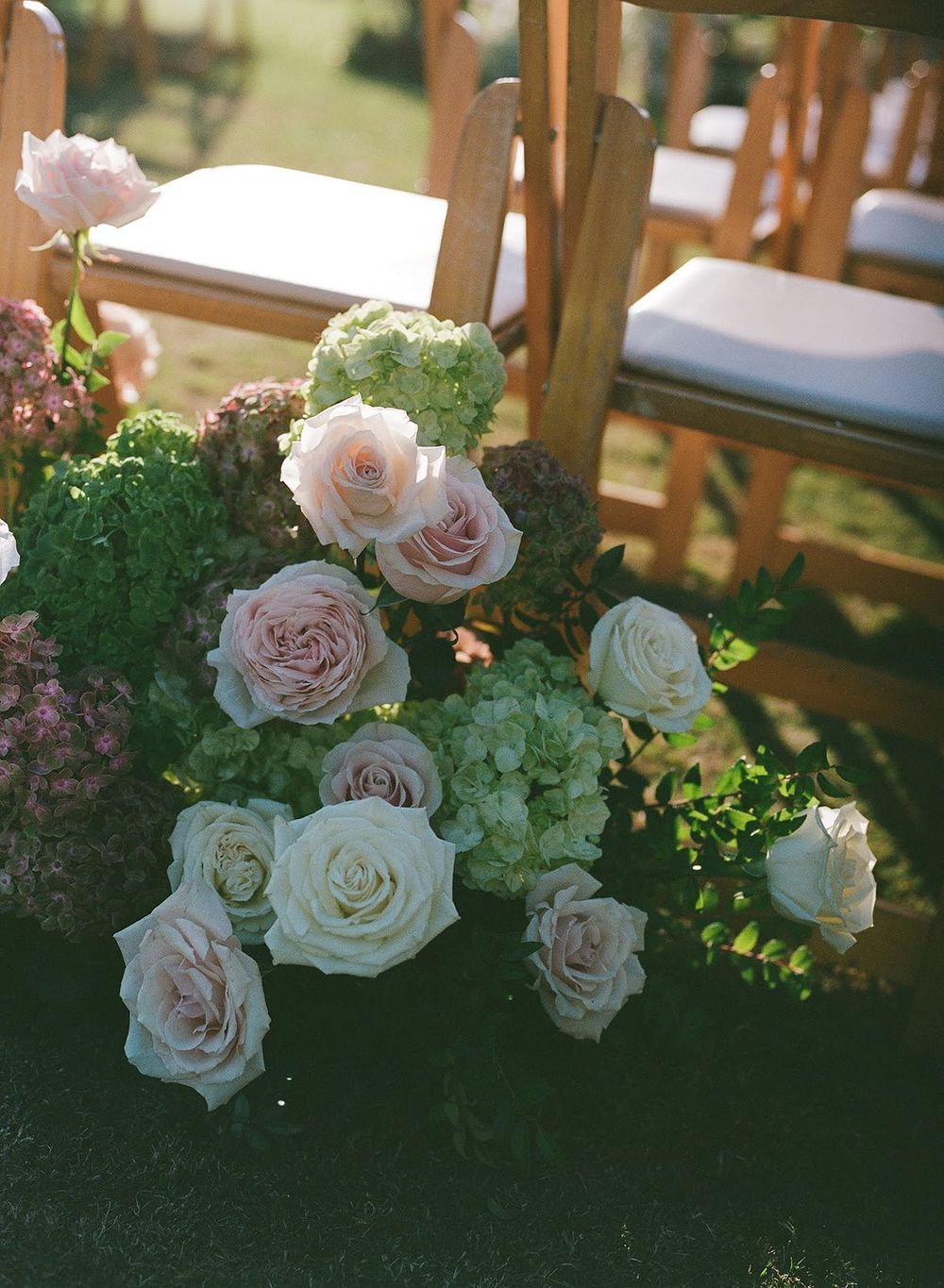 Lush floral arrangement featuring white and blush roses with greenery decorating an outdoor event space.