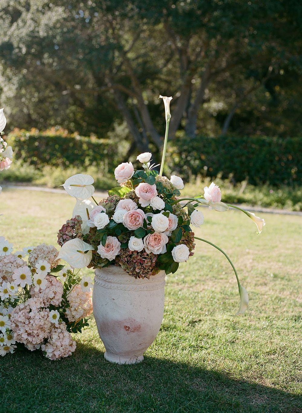 Elegant floral arrangements with pink and white blooms displayed in weathered stone vases on grass.