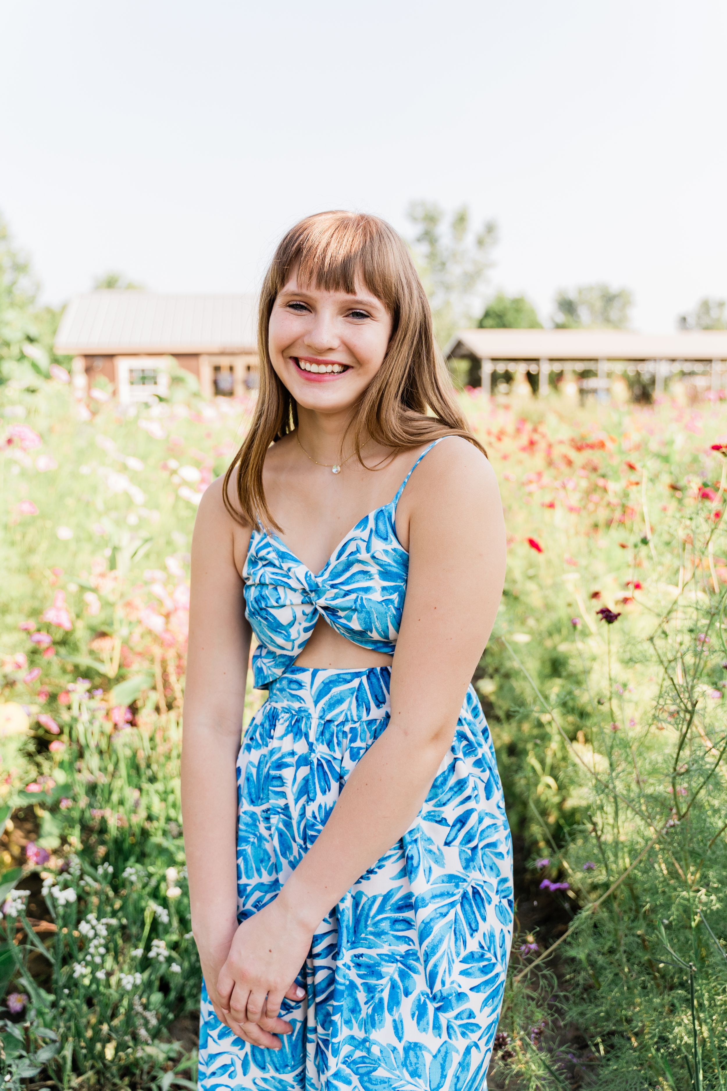 A person wearing a blue and white tropical print dress poses in a wildflower field on a sunny day.