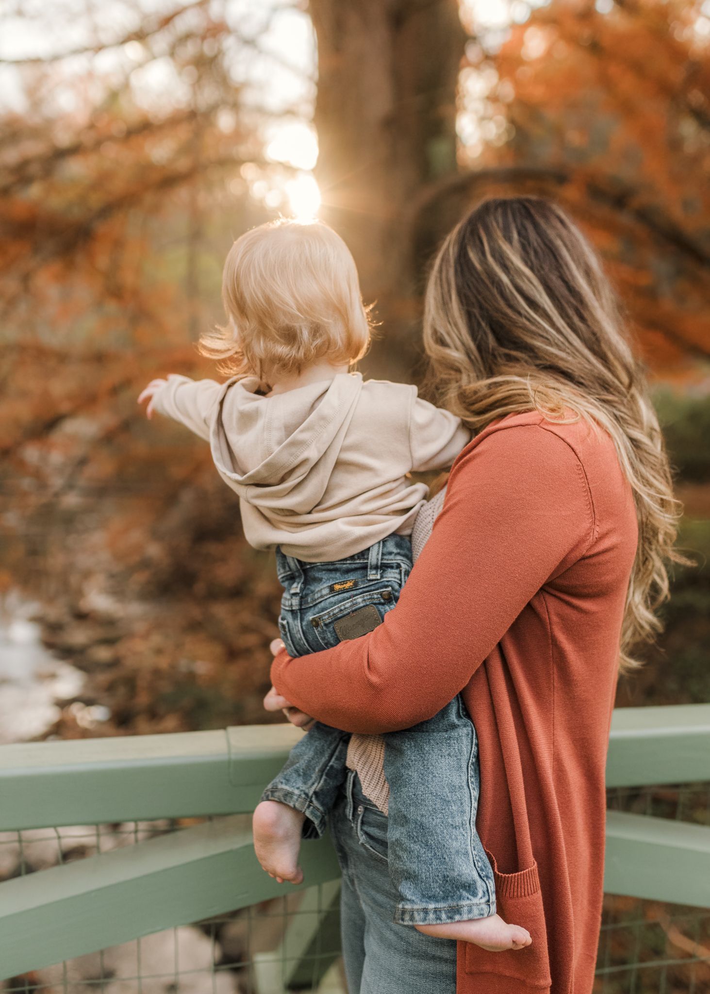 A tender embrace between parent and child is captured against a backdrop of autumn trees at sunset.