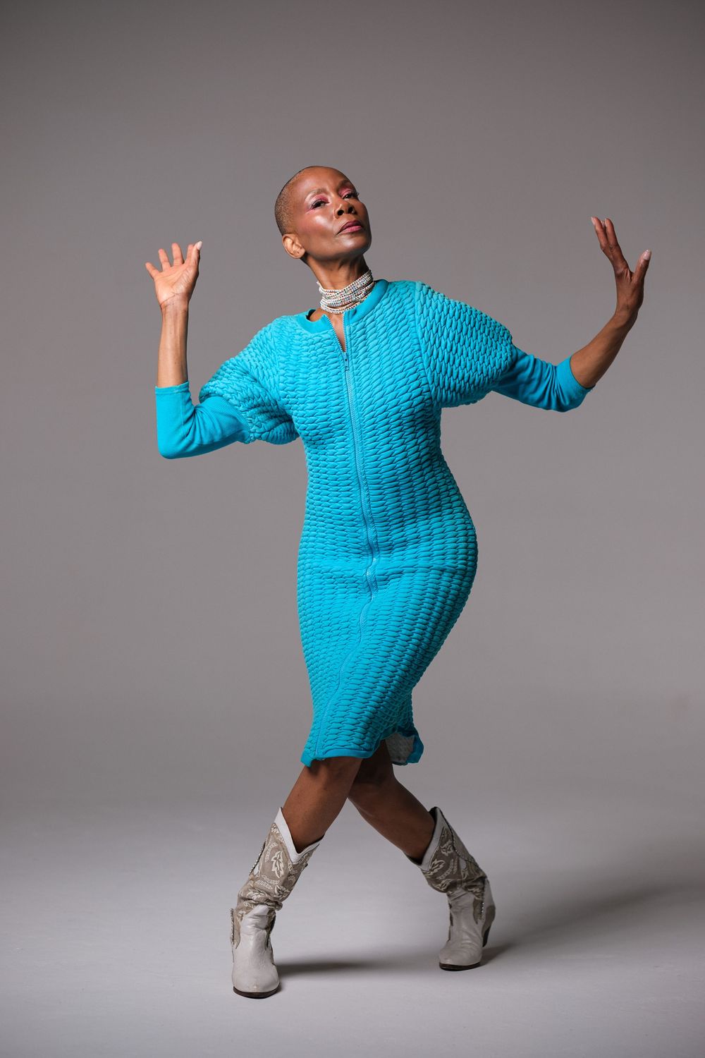 Expressive movement captured in turquoise knit dress and white boots.