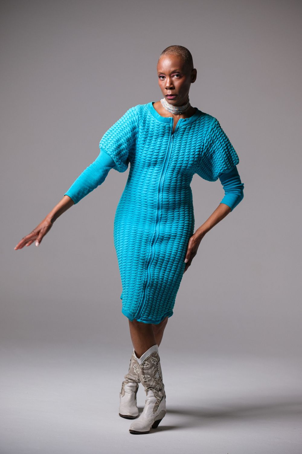 Dynamic motion shot featuring bright blue sweater dress and white boots.