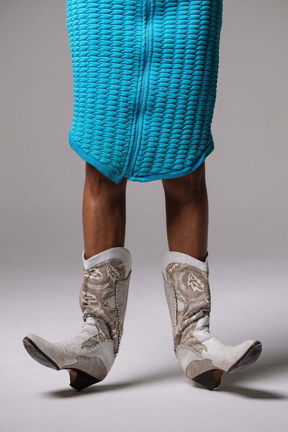 Close-up detail of white cowboy boots paired with bright turquoise knit dress.