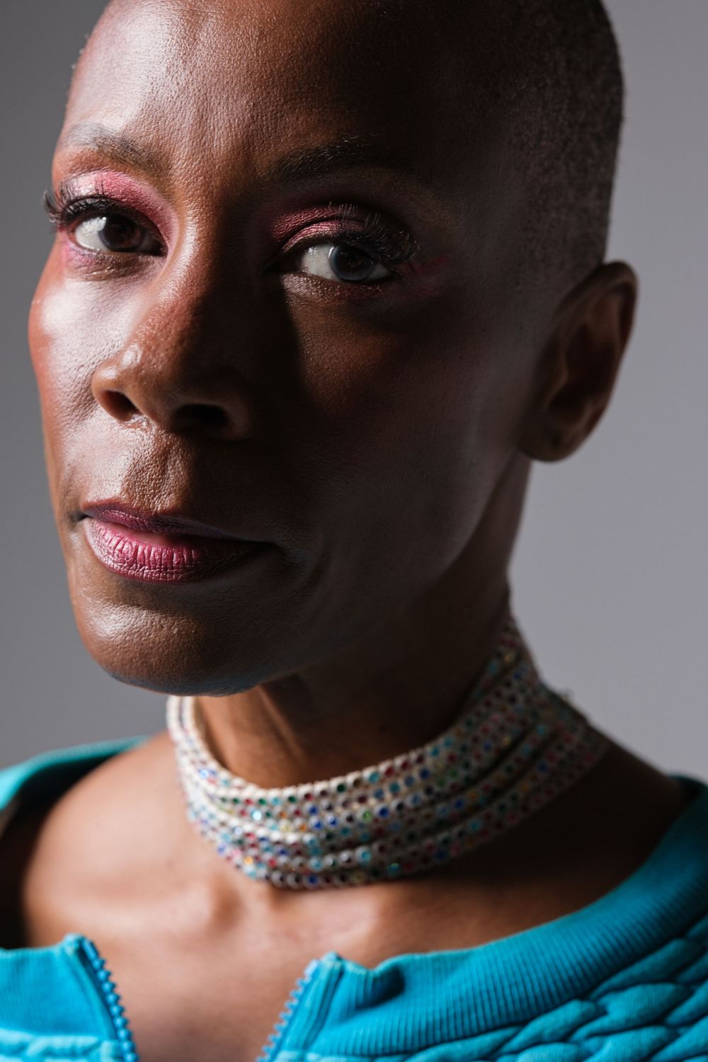 Studio portrait featuring elegant jewelry and a turquoise top against a dark background.