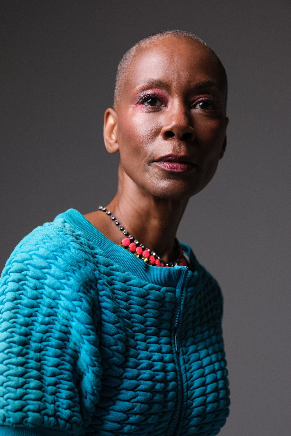 Close-up portrait showcasing a textured turquoise sweater and coral necklace.