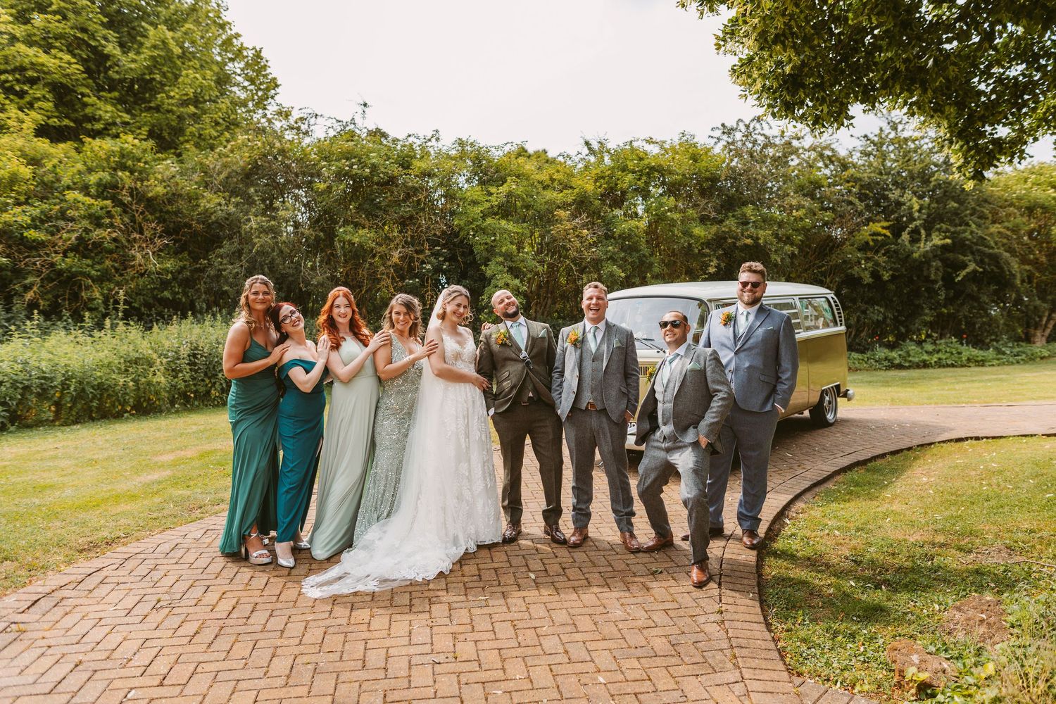 Wedding party walking and laughing together on a garden path during outdoor celebration.
