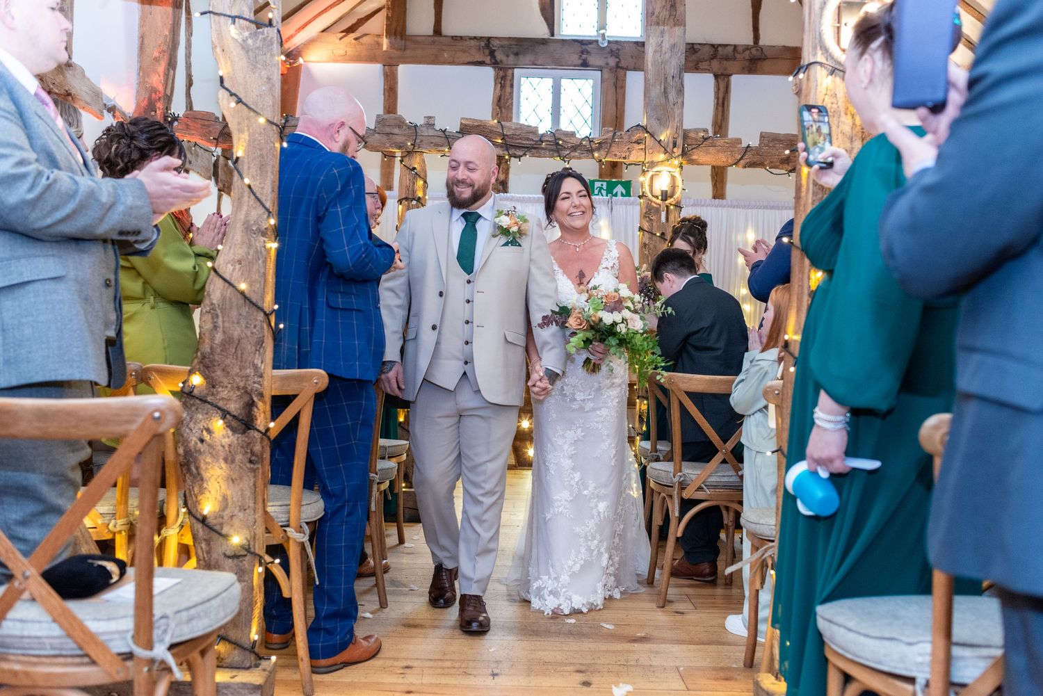 Wedding guests dancing and celebrating together on a rustic wooden dance floor at an indoor reception venue.