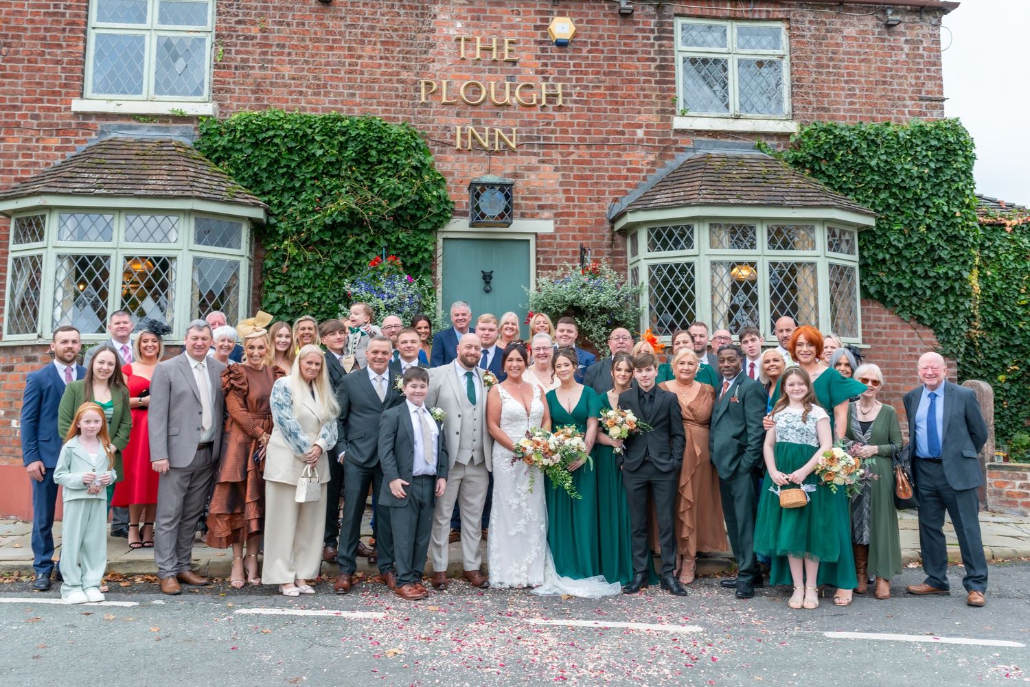 Large group wedding photo outside The Black Swan Inn with brick facade and ivy covered walls.