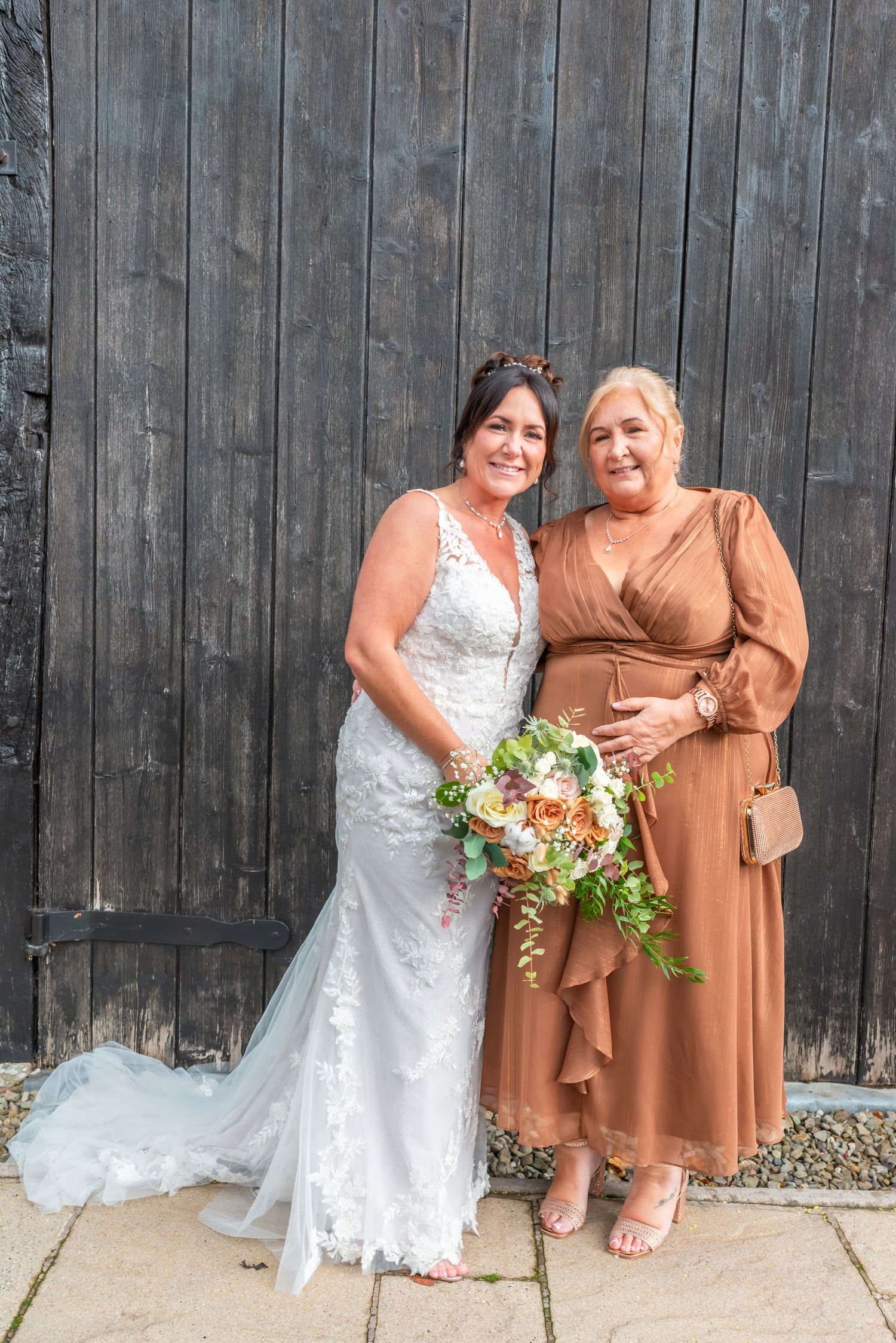 Wedding party poses against rustic wooden wall with white dress and brown attire creating elegant contrast.