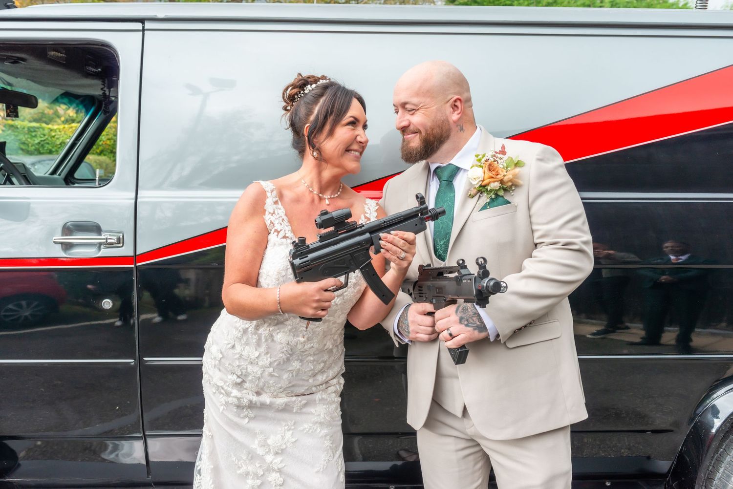A couple shares a joyful moment beside a red and black limousine on their special day.
