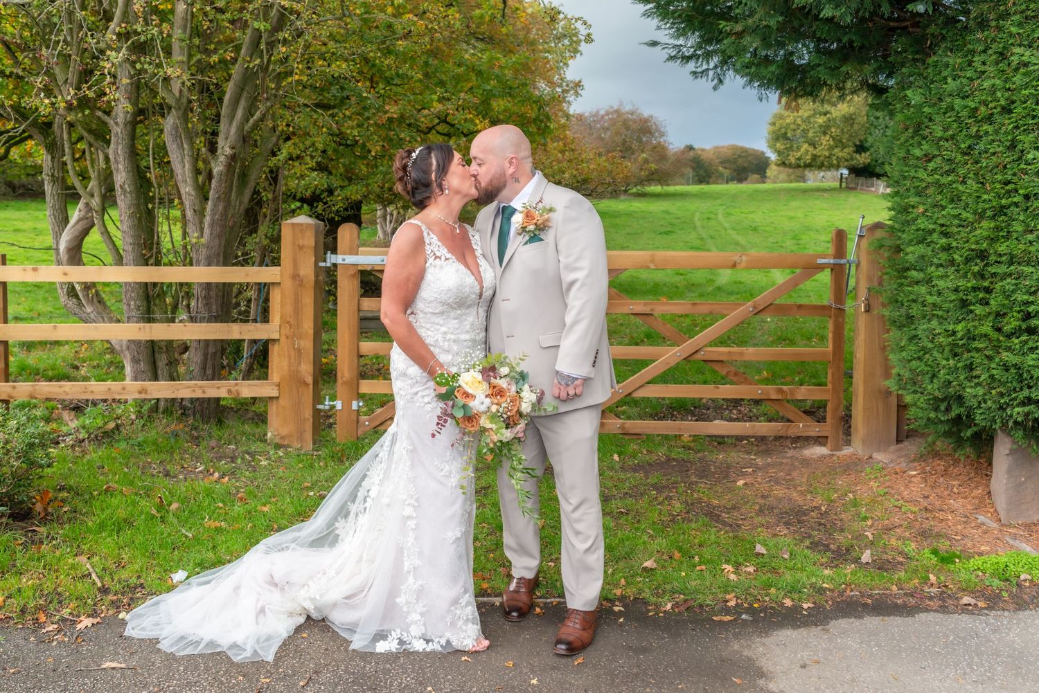 Wedding couple poses along wooden fence in outdoor garden setting with lush greenery.