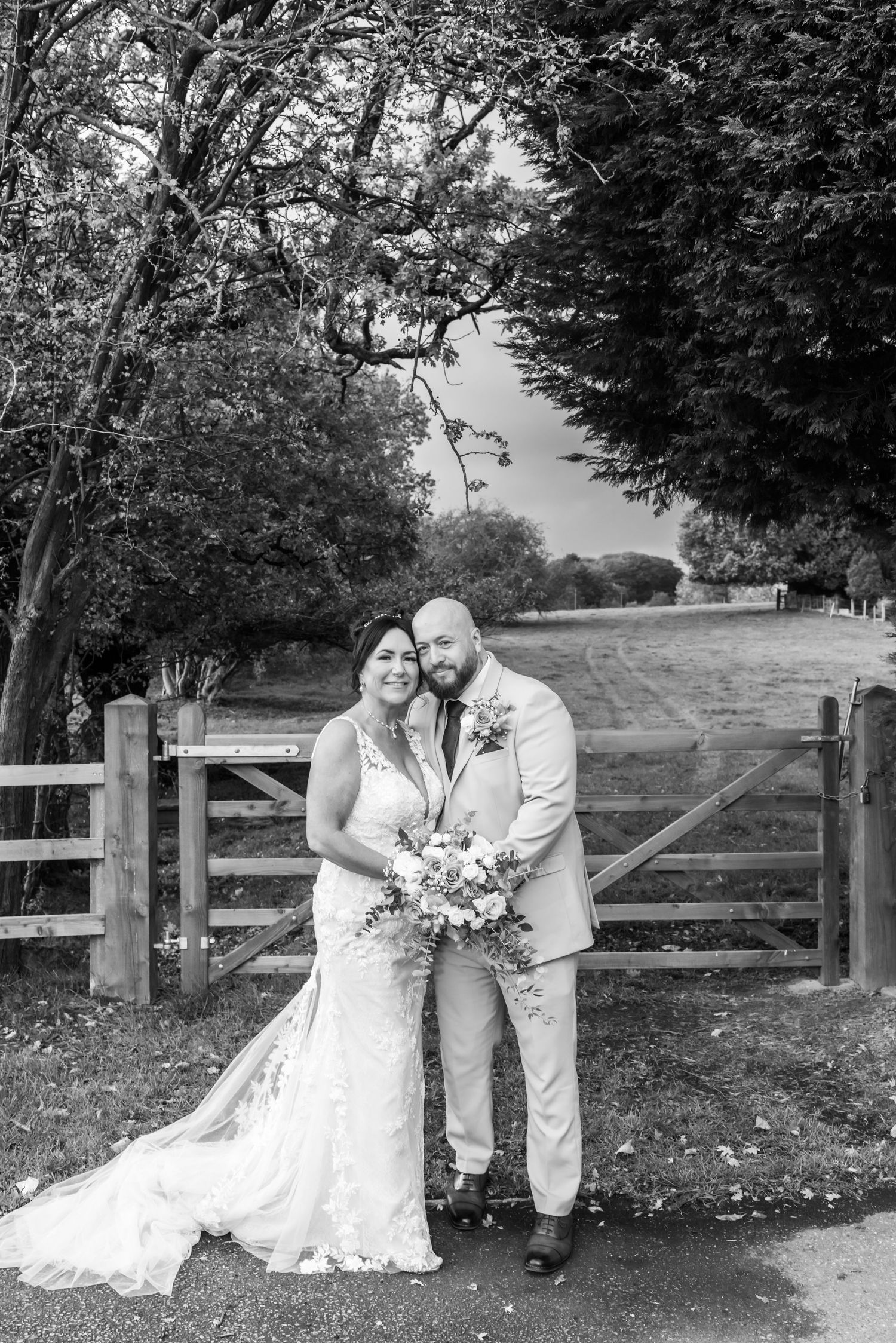 Black and white wedding photos captured along a rustic wooden fence in a countryside setting.