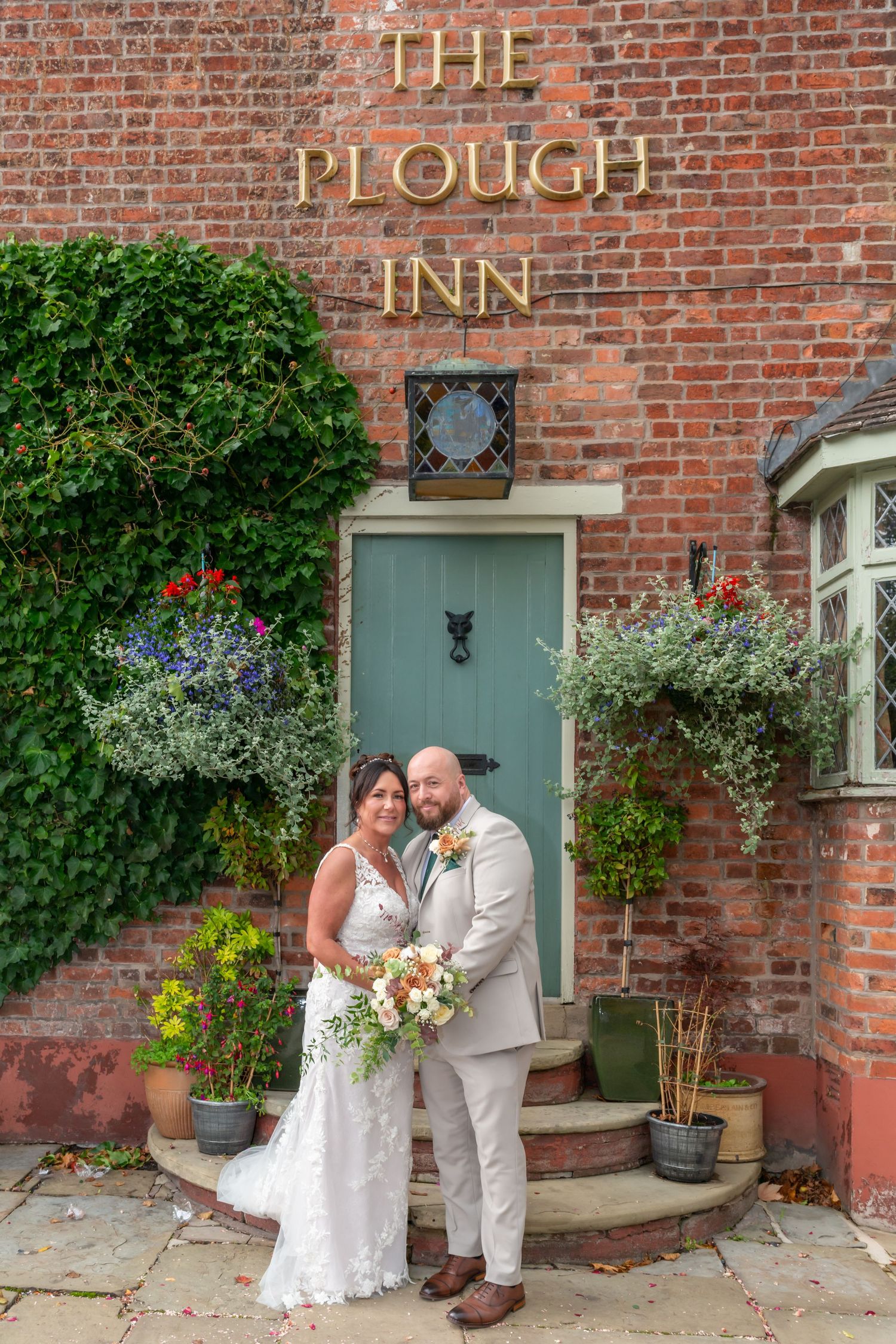 Couple posing for romantic photos outside The Plough Inn with brick walls and flowering plants.