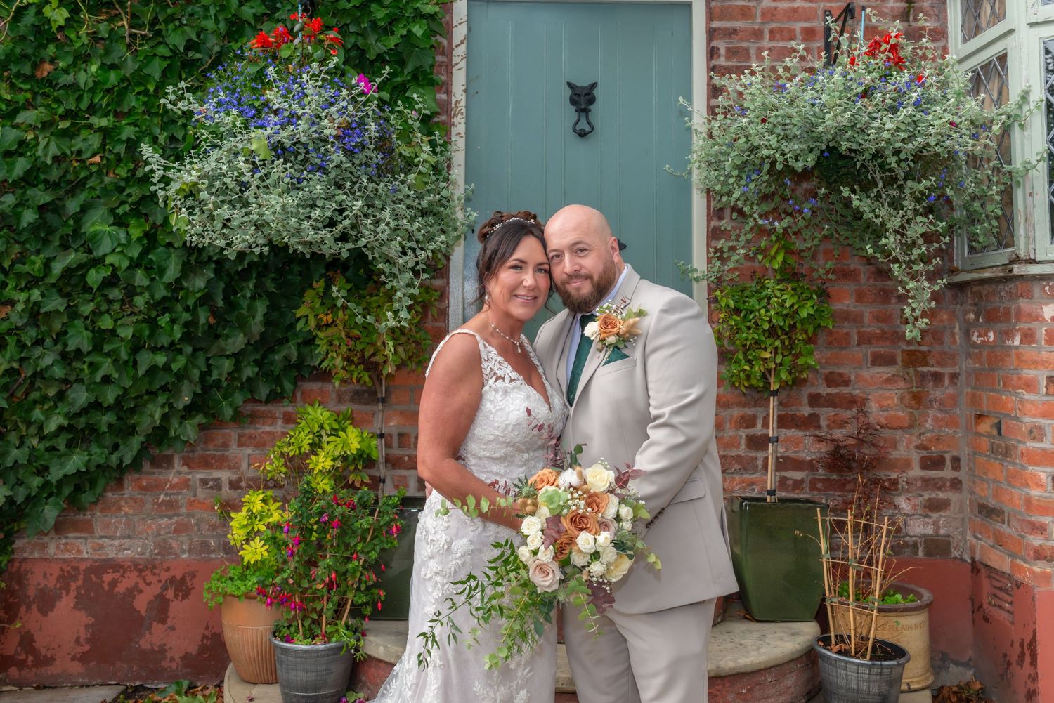 Wedding portraits against brick wall with climbing vines and blue door creating romantic backdrop.