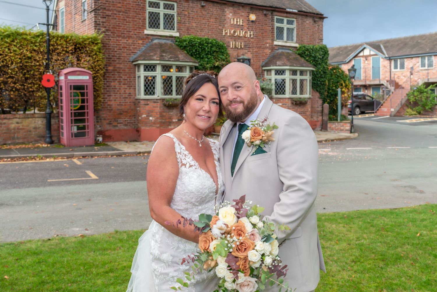 Wedding couple shares romantic moment in front of red brick building with landscaped grounds.