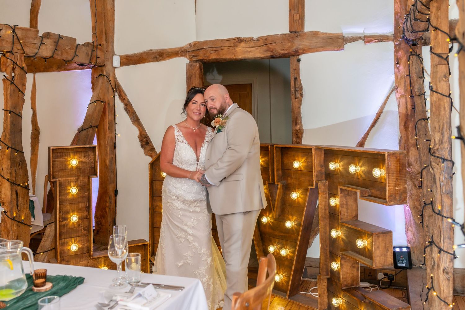 Rustic barn wedding venue interior with exposed wooden beams and twinkling lights creating warm ambiance.