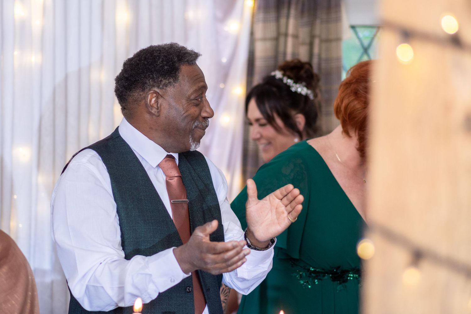 Wedding guest in a vest and tie enjoying the reception celebration with festive lights in background.