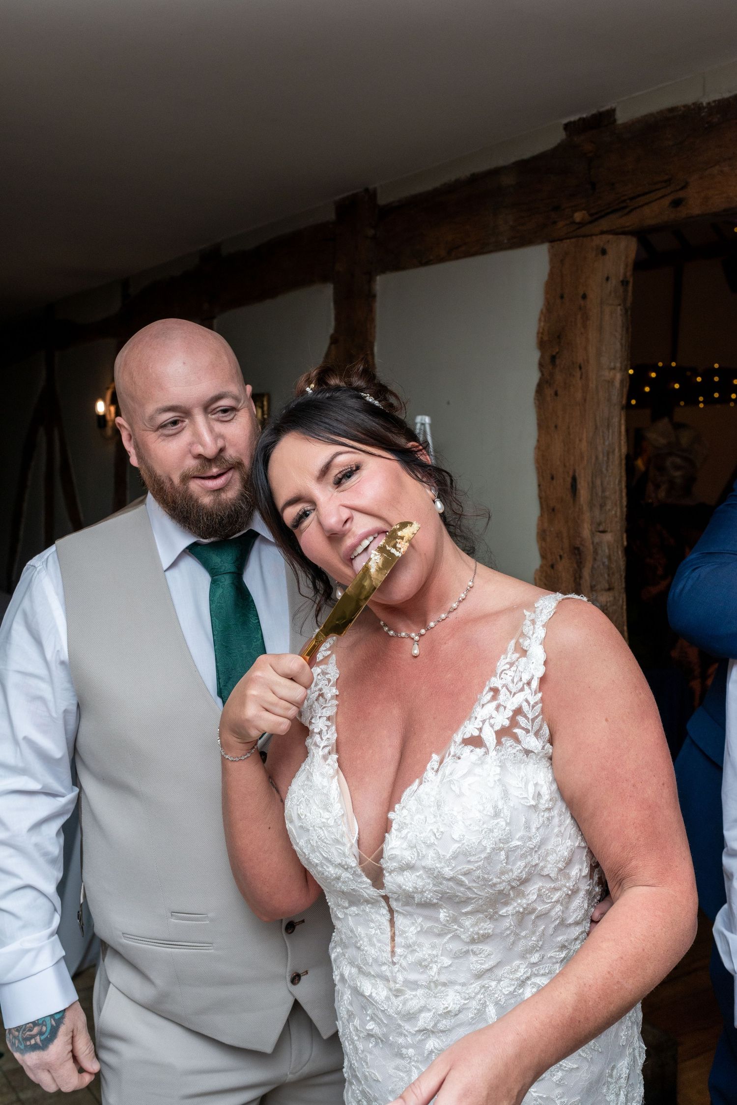 A couple at a rustic wedding venue share a playful moment with a white lace dress and emerald green tie.