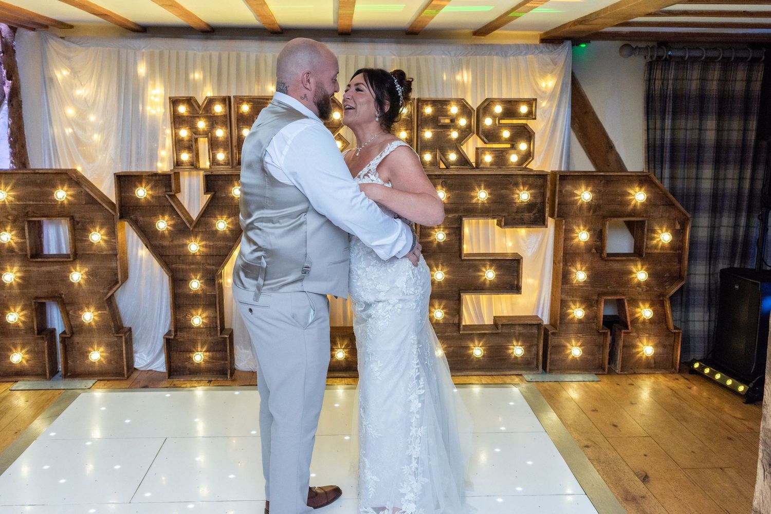 Newlyweds dancing in front of illuminated LOVE marquee letters at their reception.