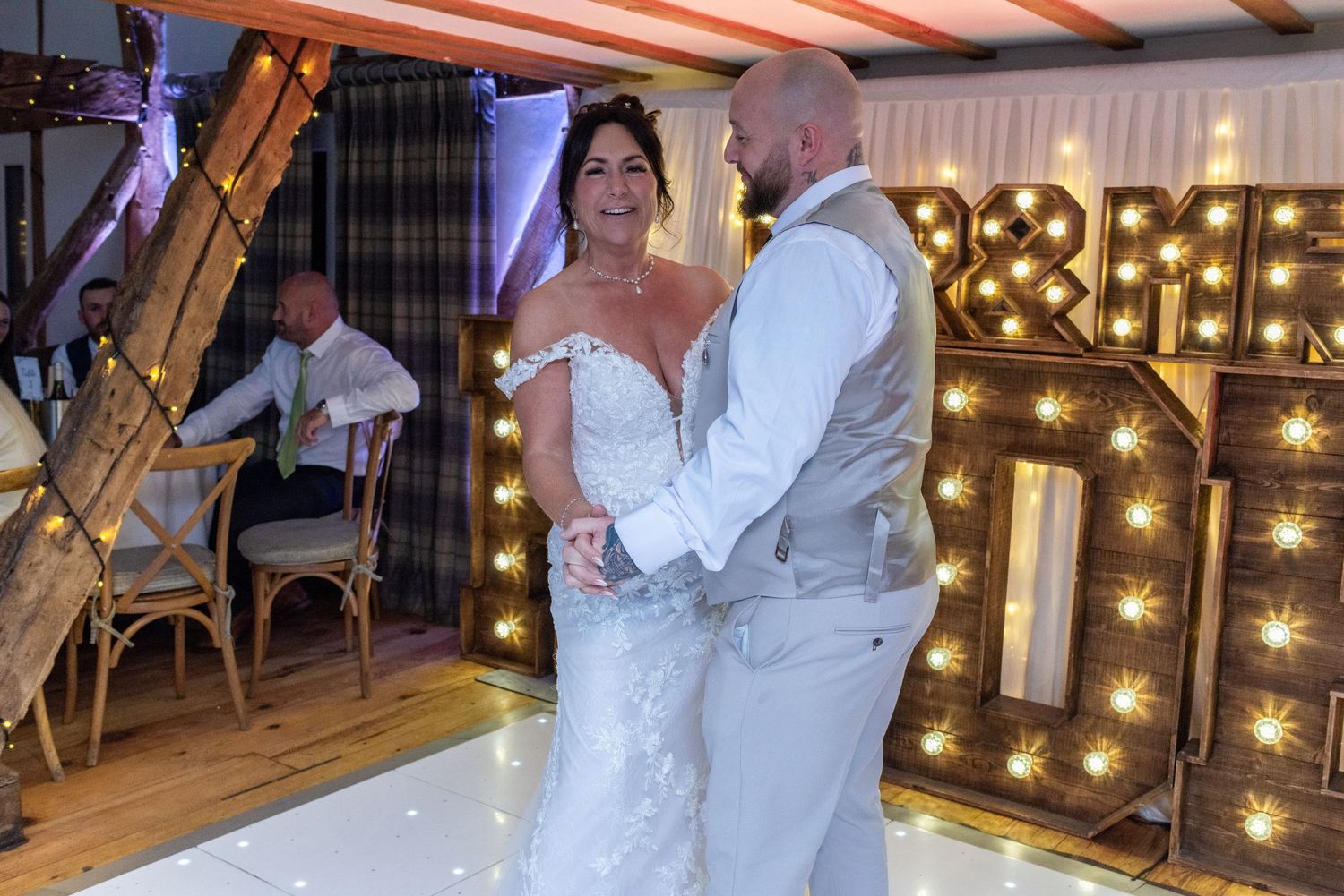 Wedding celebration on dance floor with illuminated decor and rustic wooden beams overhead.