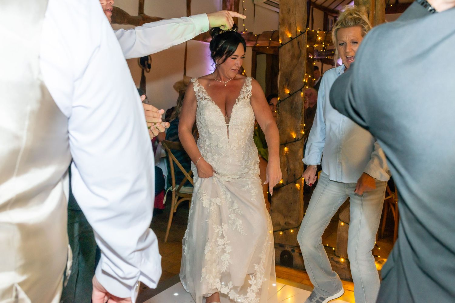 Wedding guests dancing and celebrating on a wooden dance floor with festive lighting.