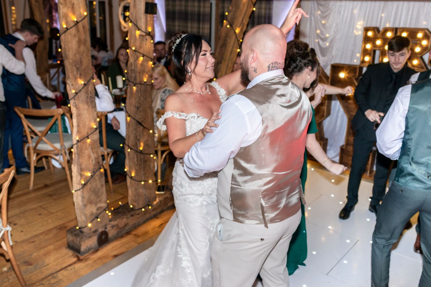 A couple dancing together at a wedding reception in a rustic barn decorated with string lights.