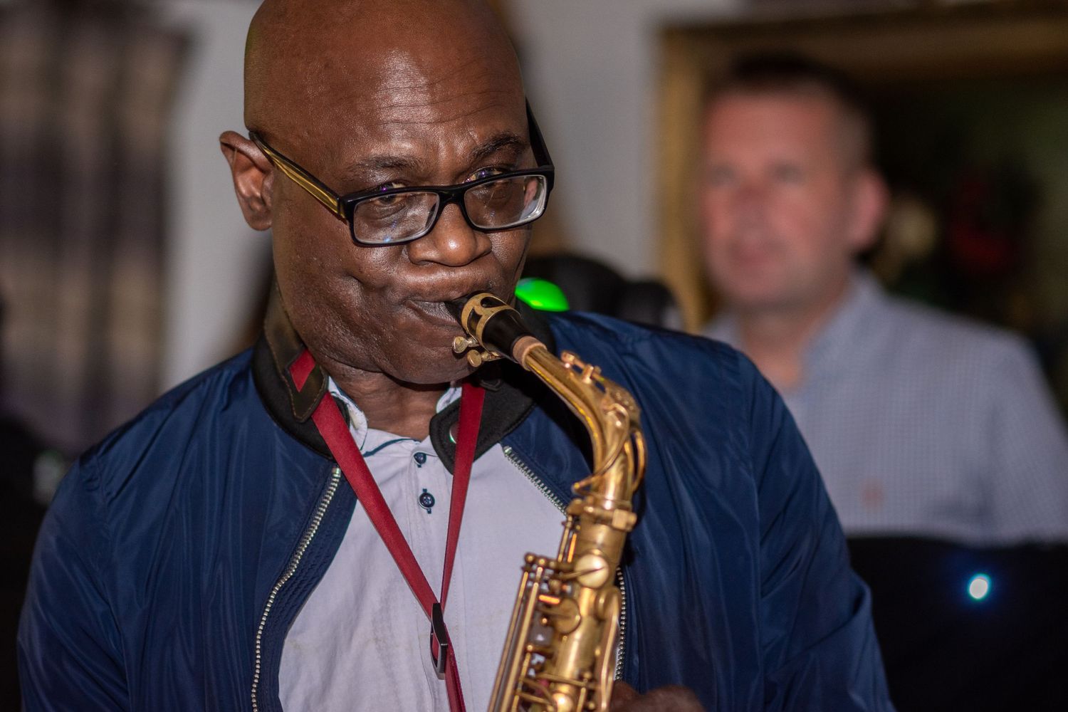 Musician playing saxophone at wedding reception wearing glasses and navy jacket.