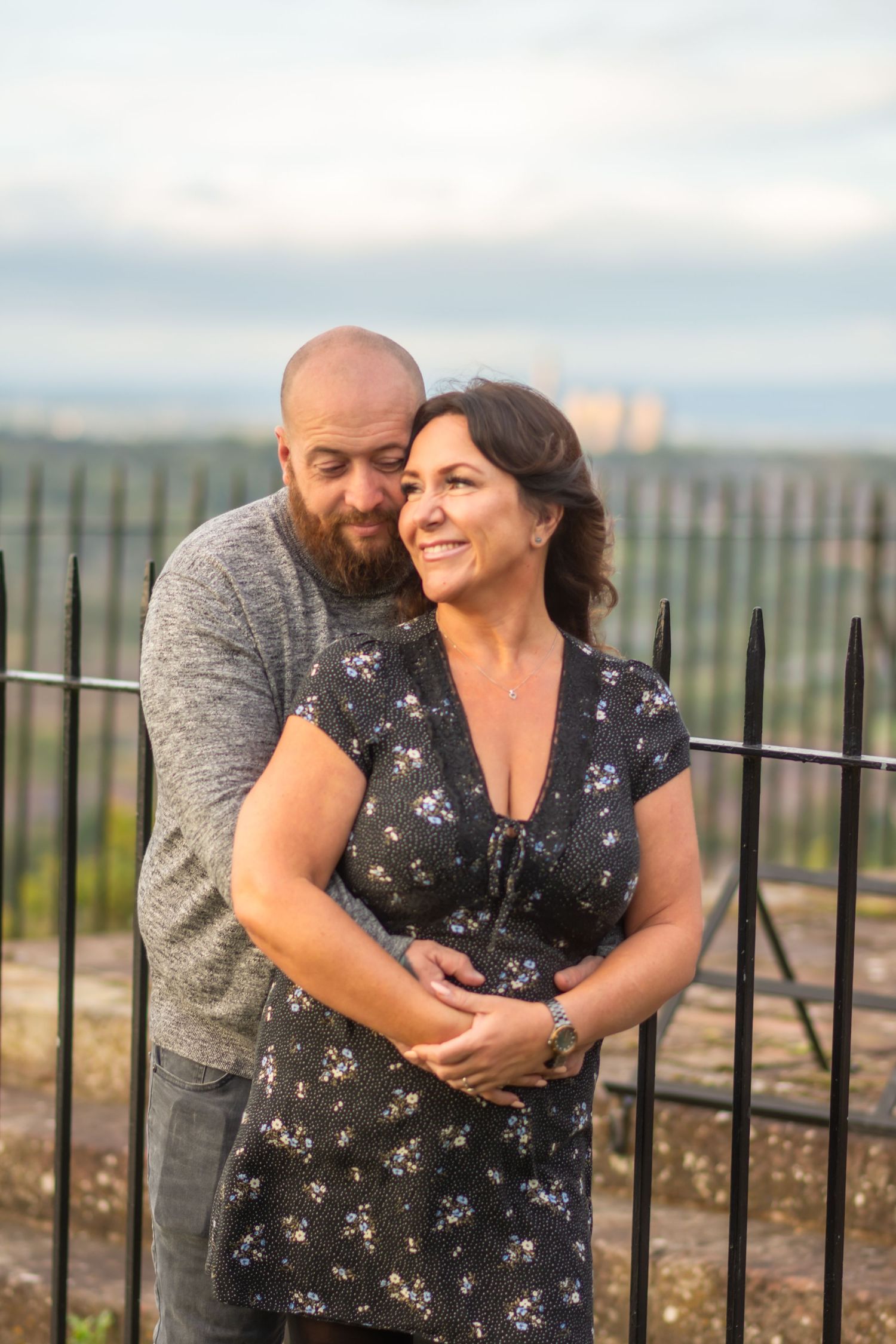 A couple embraces lovingly against an iron railing during a romantic outdoor photoshoot at sunset.