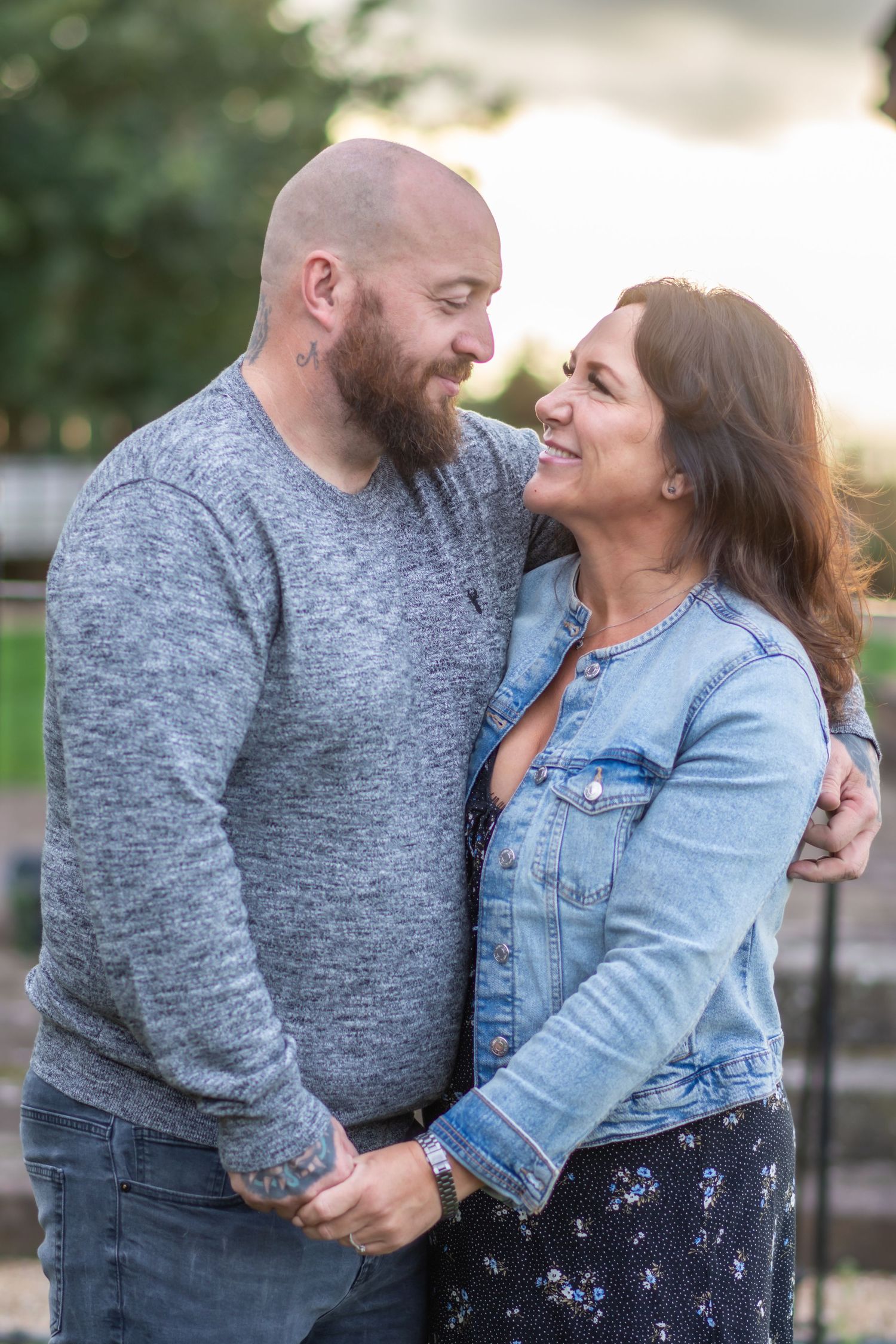 A couple shares an intimate moment outdoors, with one wearing a gray sweater and the other in a denim jacket.