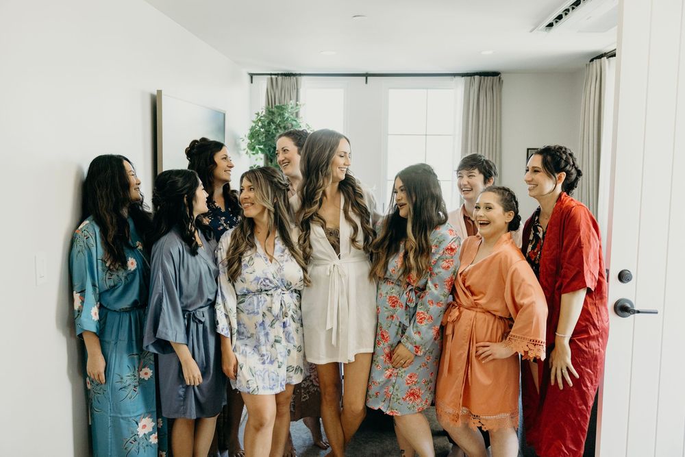 Group of bridesmaids in burgundy dresses gathered in a bright room.