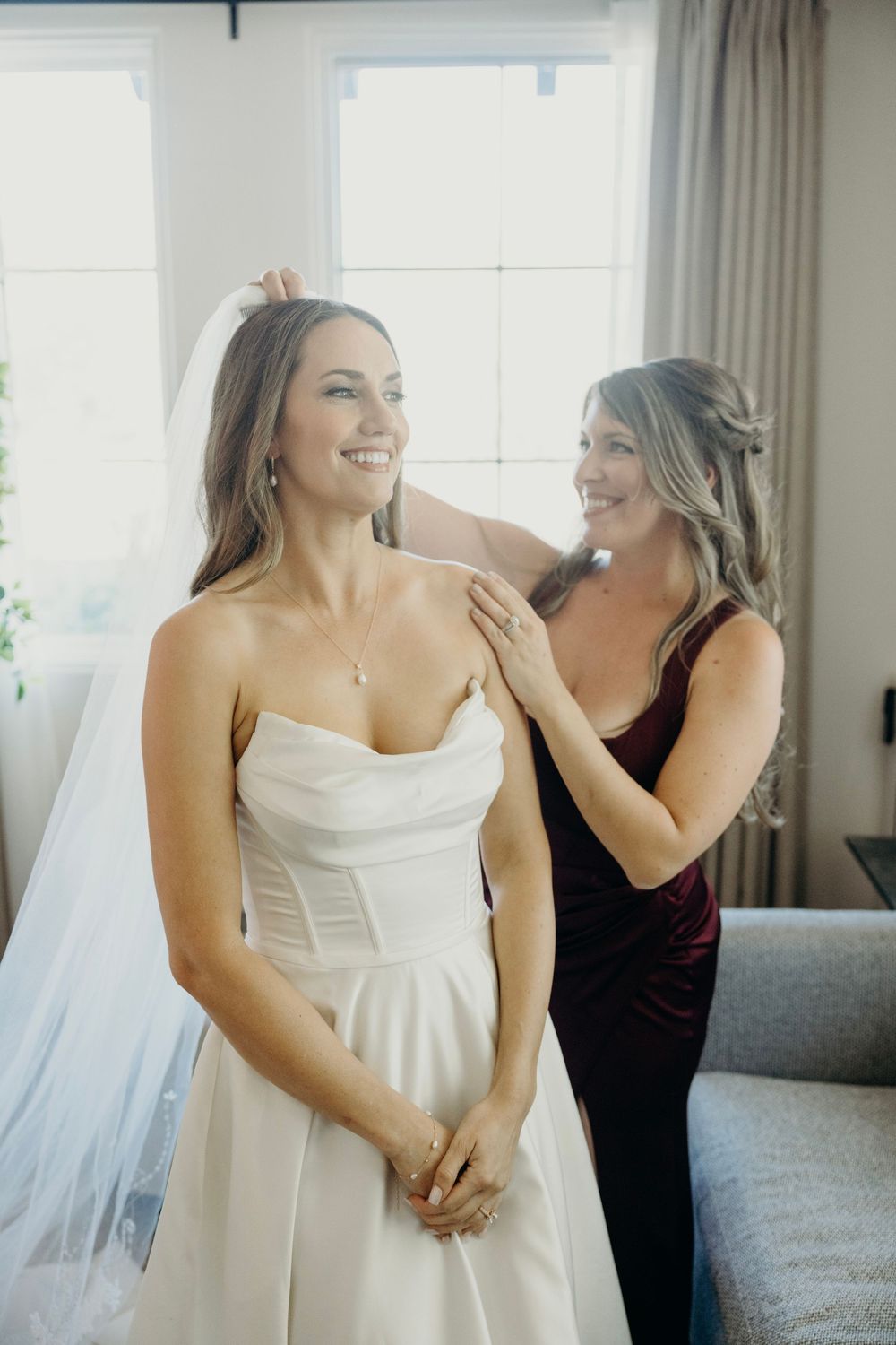 Candid moments of wedding preparation with bride in white dress and attendant in burgundy.
