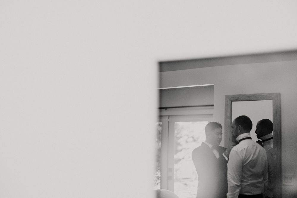 Groomsmen getting ready in a bright modern room with white walls and wooden accents.