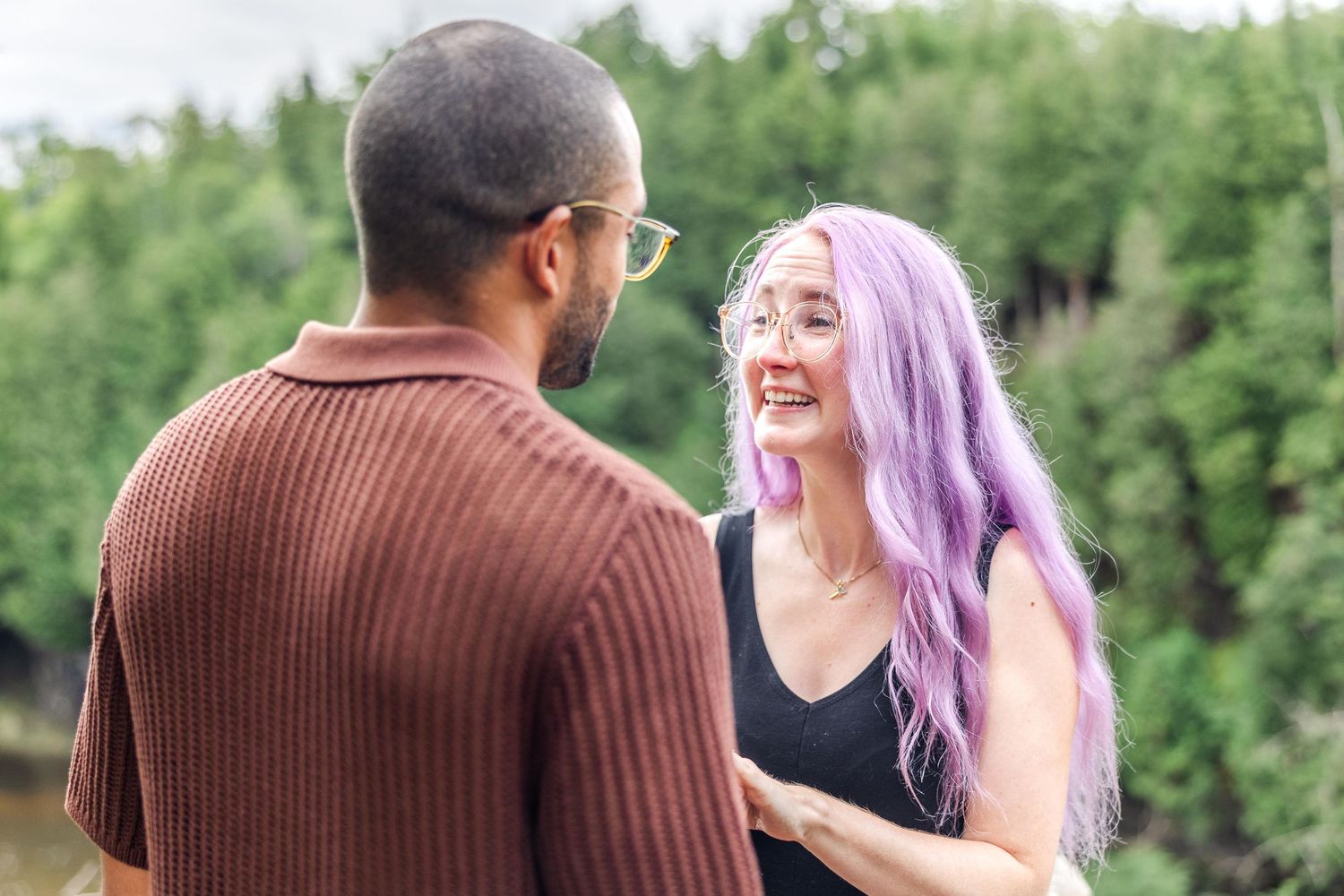A couple shares a joyful moment outdoors with lush greenery in the background.