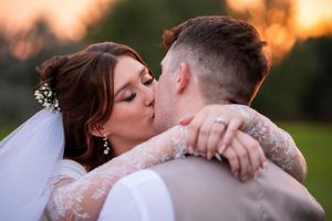 A couple shares a romantic kiss during sunset in a garden setting while wearing elegant wedding attire.