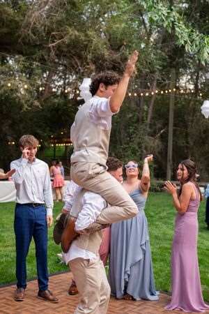 People celebrate at an outdoor wedding reception with dancing and jumping on a brick patio under string lights.