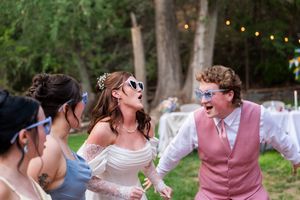 Wedding party members dancing and celebrating at an outdoor reception with string lights overhead.