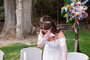 An emotional moment in a white dress at an outdoor wedding ceremony with colorful floral decorations.