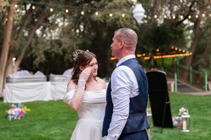 Guests enjoying a festive outdoor wedding reception under trees with string lights illuminating the space.